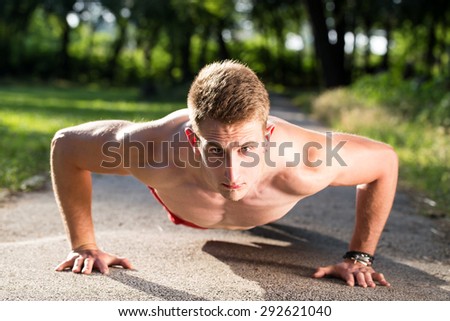 young muscular man push ups on walking road in a park
