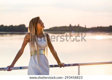 pretty dressed young girl looking up at a lake at sunset