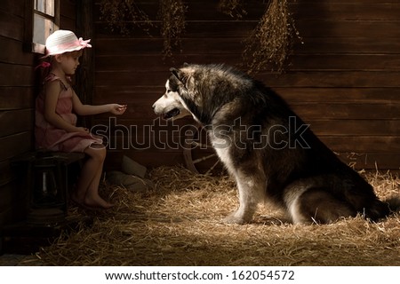 Little girl with a big dog in a barn on straw