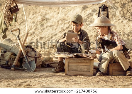 Two children archaeologists after excavations take notes in a notebook in a summer tent on a hot afternoon