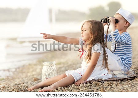 Boy with a girl sitting on the beach with binoculars and looking into the distance on a sunny summer afternoon lake