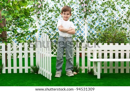 Little boy near the fence in the garden in summer sunny day