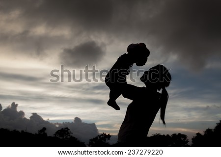 Daughter in her mother's arms silhouetted at cloud of bad weather at Thailand. Mother's & baby is motion-blurred.