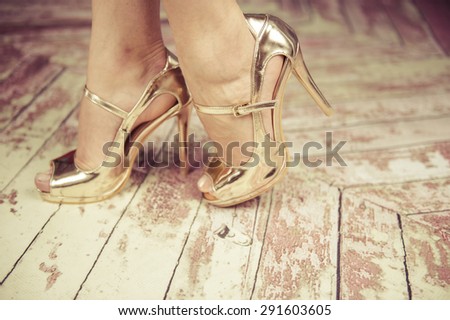 Beautiful female feet wearing golden shoes on high heels walking on the retro wooden floor.