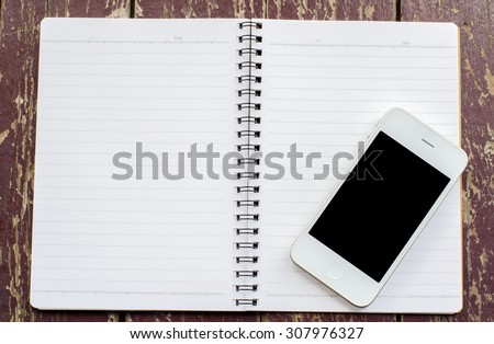 White smart phone with black screen and open Notebook on old dirty wooden background - vintage tone