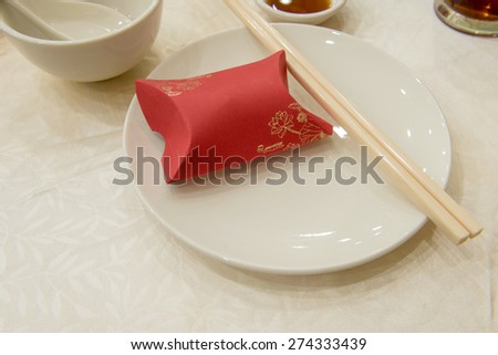 Basic eating utensils of chinese formal meal of plate, chopsticks, small soup bowl and soup spoon.  A gift box of red color is placed on the plate for guest.  Text can be insert onto the box .