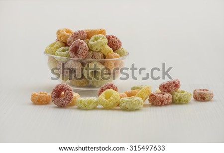 Closeup view of colorful loose cereal at the foreground and a transparent bowl full of cereal at the background on white.  The respective color have its own flavor and nutritional benefits.