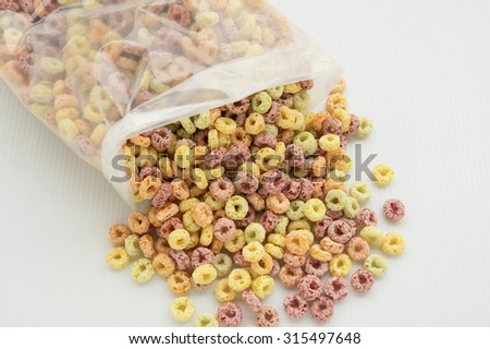Overflow breakfast cereal from a clear plastic packing.  Colorful cereal spread out on white background.