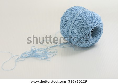 A ball of used blue acrylic yarn rolled out with loose ends created some knots.  White background.