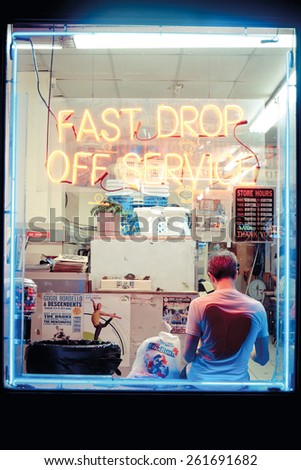 Brooklyn, New York, United States - 18 August 2015 : Hipster young man in a laundry shop, reading in front of the window in Williamsburg