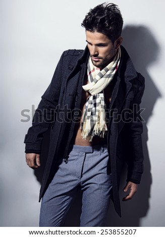 handsome young man in coat and scarf with fit body posing on grey background