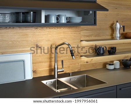 Modern kitchen with black furniture and wooden wall, black worktop have Stainless steel undermount kitchen sink and Tap water in the kitchen. dark tone kitchen