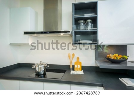 Modern white kitchen with black granite countertops and white cabinet. Have modern black induction hob, cooker, chimney extractor hood 90cm. in kitchen. Grey open shelf wall cabinet. ストックフォト © 