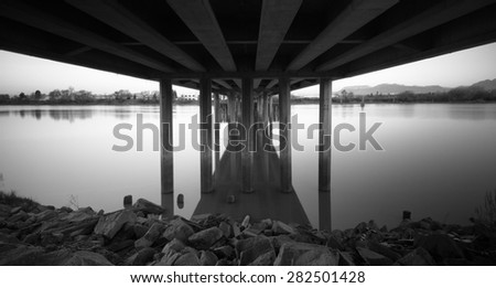 Black and white image of still water and rocks sitting under a street bridge in Vancouver, Canada on an early Sunday morning\
Location: Vancouver, Canada
