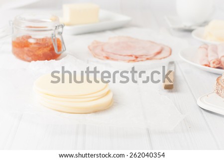 sliced of cheese served for breakfast with cold cuts, jam and bread at the background, short depth of field