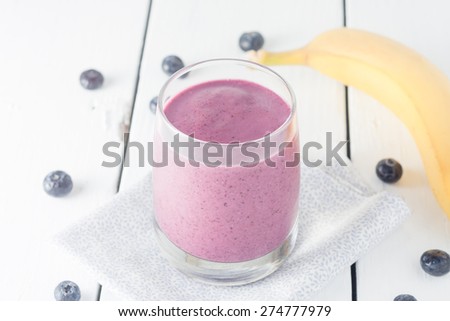 a glass of homemade banana and blueberry smoothie on white background