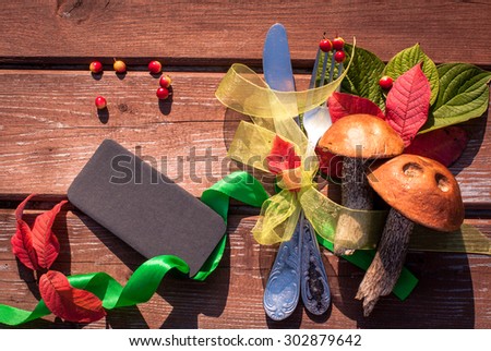 Autumn border from mushrooms, berries, cutlery and fallen leaves on old wooden table. Thanksgiving day concept. Background with tag/ sticker/ with copy space for your text. Happy Thanksgiving day.