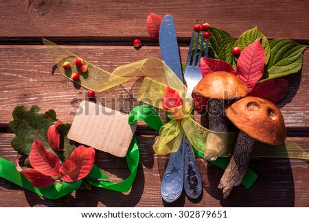 Autumn border from mushrooms, berries, cutlery and fallen leaves on old wooden table. Thanksgiving day concept. Background with tag/ sticker/ with copy space for your text. Happy Thanksgiving day.