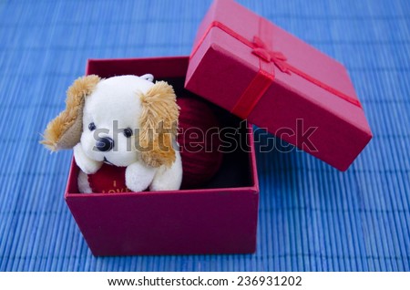 A toy dog in a red present box with a ribbon, on blue background