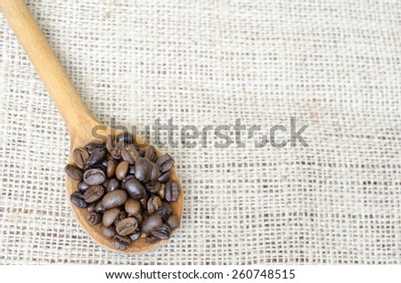 Wooden spoon full with roasted coffee beans on a vintage tablecloth