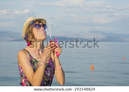 Young girl blowing soap bubbles at the beach by the sea wearing straw hat and sunglasses