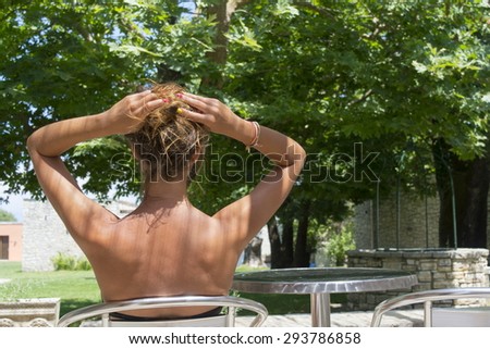 Young tanned girl sitting in a beautiful backyard wearing bikini with her hair lifted up
