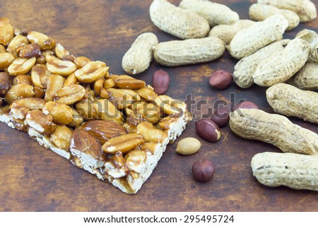 Honey bar with peanuts almonds and hazelnuts surrounded by bunch of roasted and raw peanuts placed on a wooden board