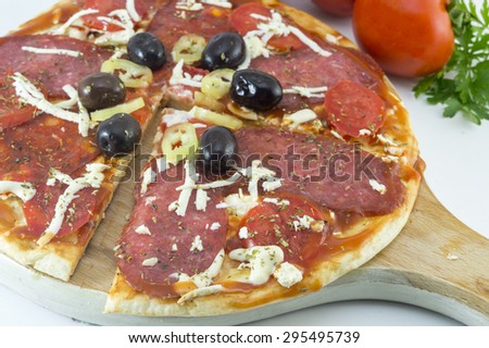 Sliced round pizza and raw tomatoe and parsley on a wooden plate