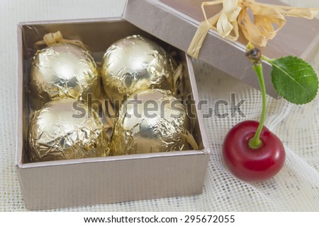 Chocolate candies wrapped in golden coloured packaging in a red present box with fresh cherries