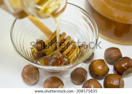 Honey dipping on hazelnuts next to a glass with honey.Healthy dessert