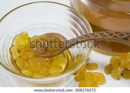 Raisins  and honey in a glass dish next to a honey jar. Healthy dessert
