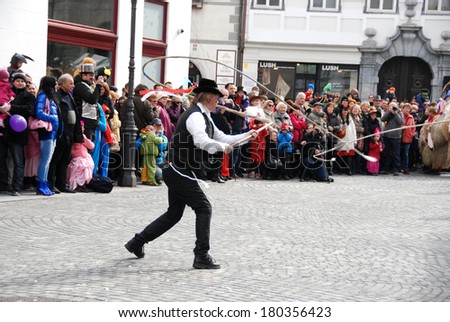 LJUBLJANA, SLOVENIA - MARCH 1, 2014: Man with great skill swivels his whip, making loud noise (children shut their ears) - traditional Slovene carnival figure -  at Dragon Carnival parade.