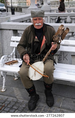 LJUBLJANA, SLOVENIA - APRIL 30, 2015: Folk musician Miroslav Matic plays on traditional Serbian string instrument gusle and sing  at Triple bridge. There is a falcon and a two-headed snake on the top.