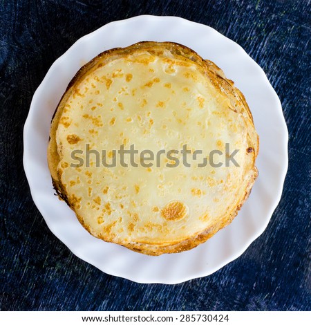 Traditional Russian Pancakes on Dark Wooden Background. Delicious breakfast meal. Top View of White Plate with Fresh Baked Homemade Pancakes.