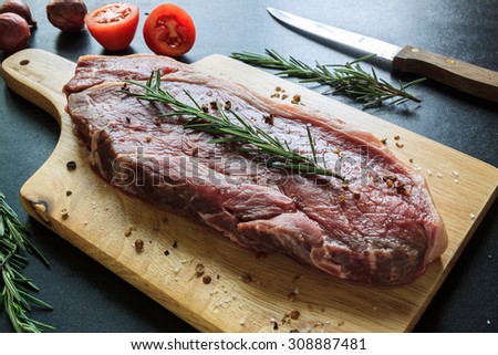 Raw meat on wood cutting board with knife tomato and rosemary