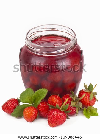 Homemade strawberry jam in a jar covered with paper, and one strawberry aside