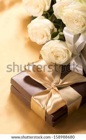 Bouquet of beautiful roses next to a gift on a gold table