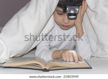 The boy has hidden under a blanket with a small lamp and reads the book