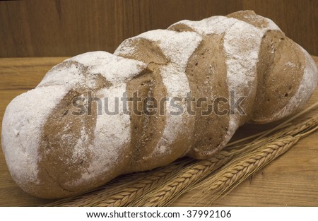 long loaf of bread and wheat ears lie on wooden board