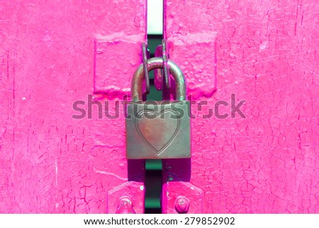 Padlocked shape of heart on pink door.