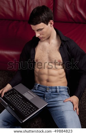 Pose of handsome sexy young man with laptop. Wearing black shirt, jeans, showing muscle body.