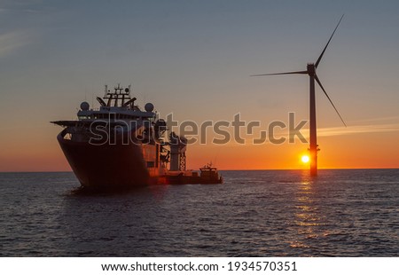 Service operational vessel, with crew transfer vessel alongside and sun setting on wind turbine