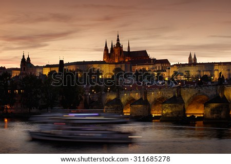The Prague Castle, gothic style,  largest ancient castle in the world, and Charles Bridge are the symbols of Czech capital, built in medieval times, moving boats, Twilight view of Prague, after sunset