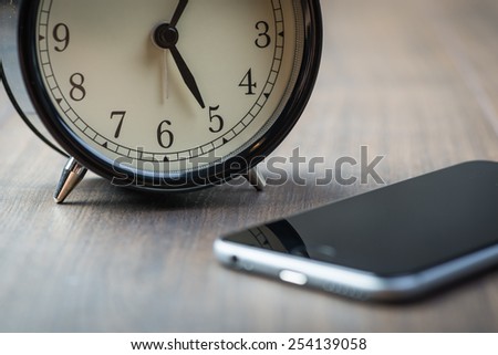 Black vintage alarm clock with phone on a wooden floor