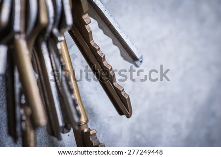 A bunch of old worn keys hanging on the screw on the grey concrete wall
