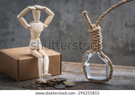 Small wooden dummy sitting with hangman\'s noose, house and coins over the grey concrete wall