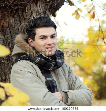 Young smiling man portrait standing in front of an autumn tree.
