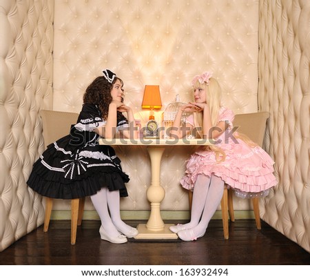 Young women dressed as dolls, sitting at a table in the doll house.