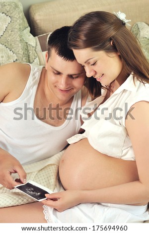 Happy couple future parents enjoy ultrasound picture of their future child at home.