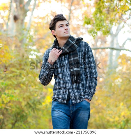 Handsome serious man dressed in a plaid scarf walking in autumn park.